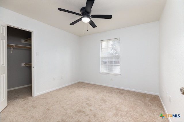 unfurnished bedroom with ceiling fan, a spacious closet, light carpet, and a closet