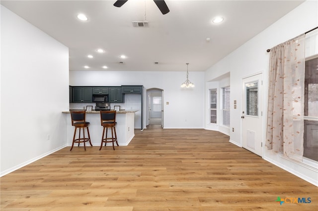 kitchen with a kitchen breakfast bar, ceiling fan with notable chandelier, decorative light fixtures, light hardwood / wood-style floors, and kitchen peninsula