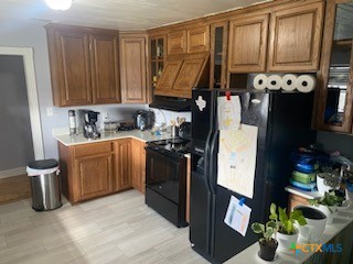 kitchen featuring light hardwood / wood-style floors, black appliances, and premium range hood