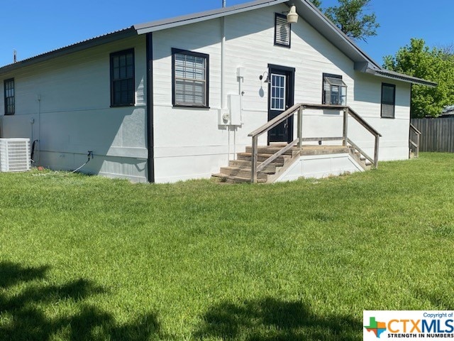 rear view of house with central air condition unit and a lawn