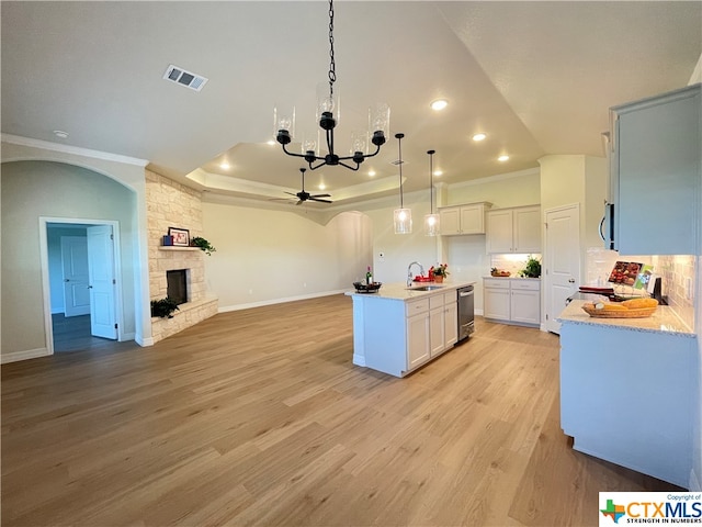 kitchen with light wood-type flooring, decorative light fixtures, a center island with sink, and white cabinets