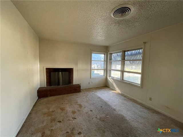 unfurnished living room with carpet flooring, a textured ceiling, and a brick fireplace