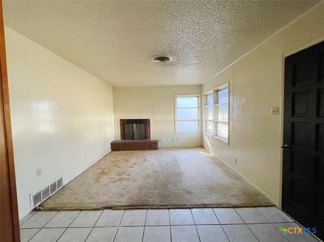 unfurnished living room featuring light colored carpet, a textured ceiling, and a brick fireplace