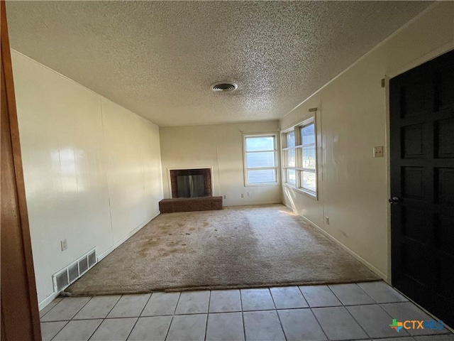 unfurnished living room featuring light colored carpet, a textured ceiling, and a brick fireplace