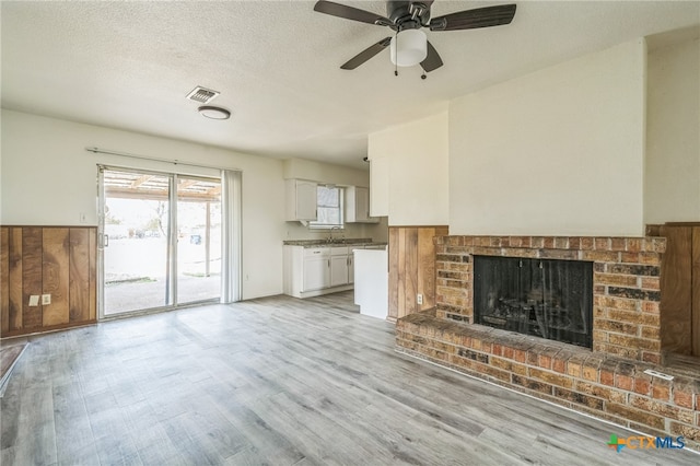 unfurnished living room featuring ceiling fan, sink, a brick fireplace, light hardwood / wood-style flooring, and a textured ceiling