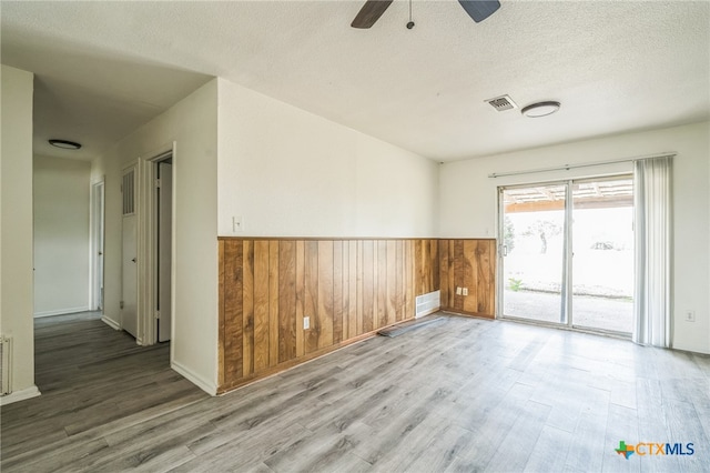 unfurnished room featuring hardwood / wood-style floors, ceiling fan, wood walls, and a textured ceiling