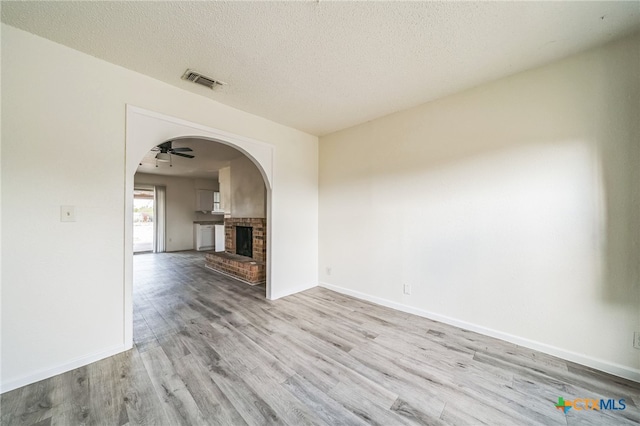 spare room featuring ceiling fan, a fireplace, light hardwood / wood-style floors, and a textured ceiling