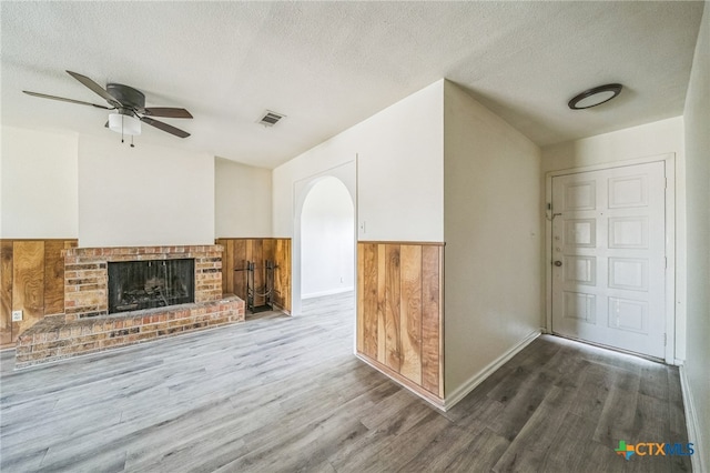 unfurnished living room with ceiling fan, hardwood / wood-style floors, a textured ceiling, and a brick fireplace