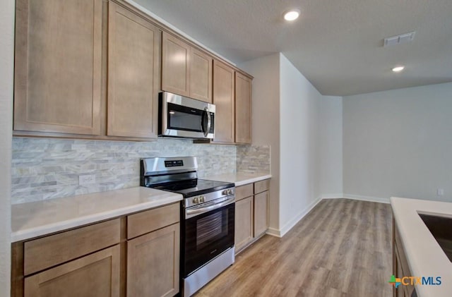 kitchen with decorative backsplash, light brown cabinets, stainless steel appliances, and light hardwood / wood-style flooring