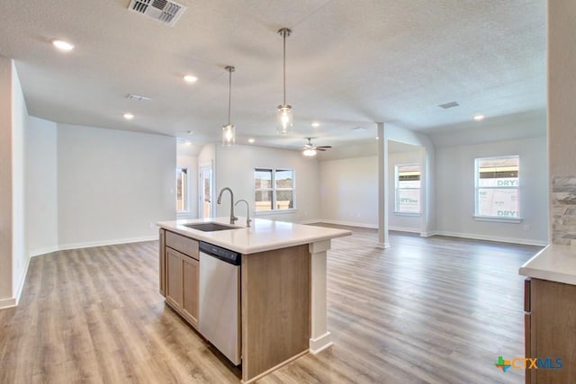 kitchen with sink, dishwasher, light hardwood / wood-style floors, hanging light fixtures, and an island with sink