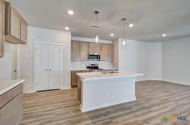 kitchen with light brown cabinets, a center island with sink, sink, decorative light fixtures, and stainless steel appliances