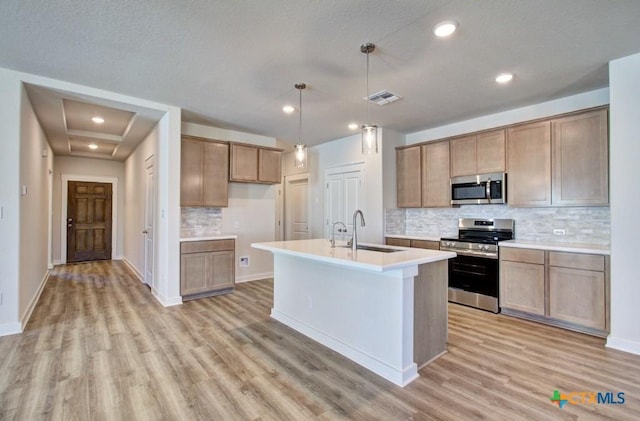 kitchen featuring sink, hanging light fixtures, an island with sink, tasteful backsplash, and stainless steel appliances