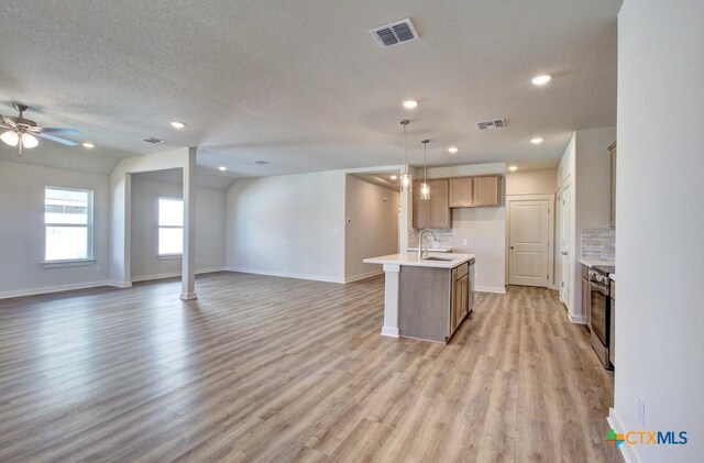 kitchen featuring ceiling fan, hanging light fixtures, lofted ceiling, decorative backsplash, and a center island with sink