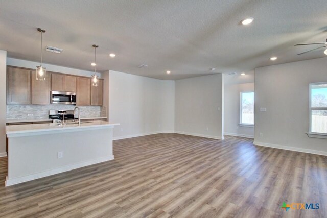 kitchen featuring ceiling fan, hanging light fixtures, wood-type flooring, decorative backsplash, and appliances with stainless steel finishes