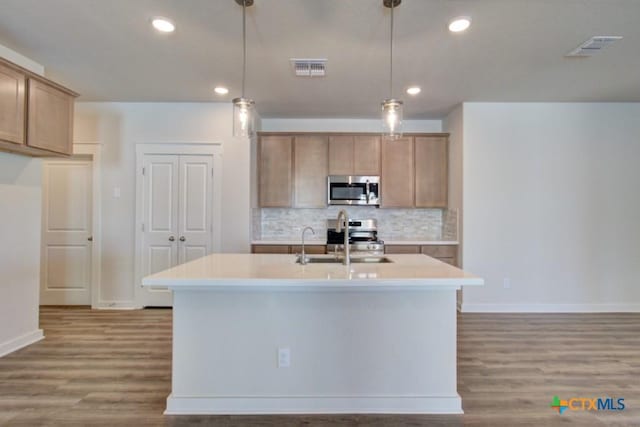 kitchen with appliances with stainless steel finishes, sink, pendant lighting, a center island with sink, and hardwood / wood-style floors