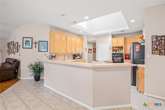 kitchen featuring light brown cabinets, kitchen peninsula, a skylight, and stainless steel fridge