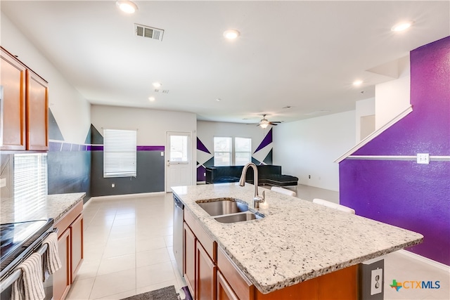 kitchen featuring a center island with sink, sink, appliances with stainless steel finishes, light stone countertops, and light tile patterned floors