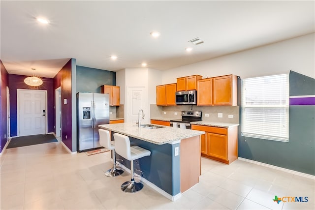 kitchen featuring light stone counters, stainless steel appliances, a kitchen bar, sink, and a kitchen island with sink