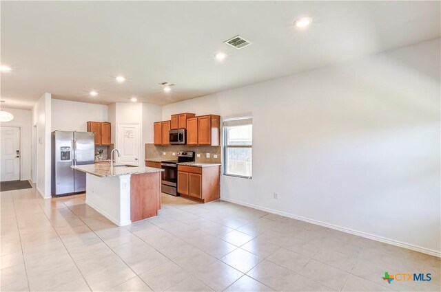 3802 Endicott Dr, Killeen, TX 76549 - kitchen with appliances with stainless steel finishes, an island with sink, tasteful backsplash, brown cabinets, and light stone countertops
