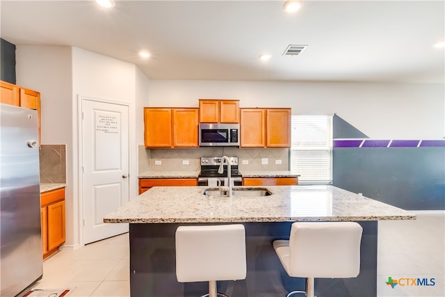 kitchen with stainless steel appliances, sink, a breakfast bar, light stone countertops, and a kitchen island with sink