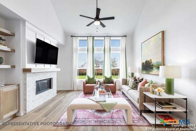 living room with a brick fireplace, ceiling fan, vaulted ceiling, and light wood-type flooring