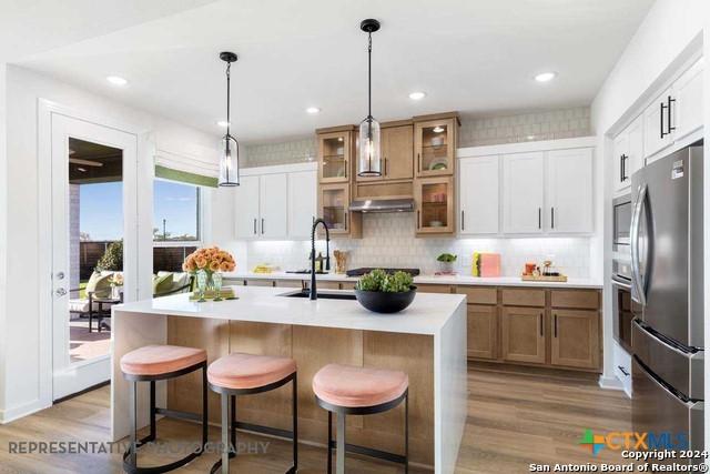 kitchen with sink, stainless steel appliances, an island with sink, light hardwood / wood-style floors, and white cabinets