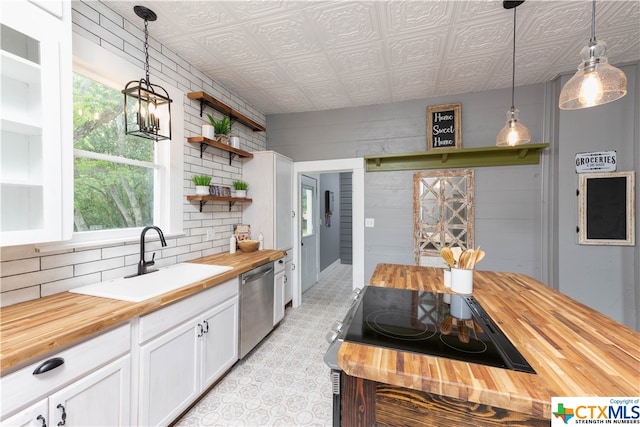 kitchen featuring white cabinets, dishwasher, sink, butcher block countertops, and pendant lighting