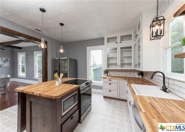 kitchen with butcher block countertops, a wealth of natural light, and white cabinets