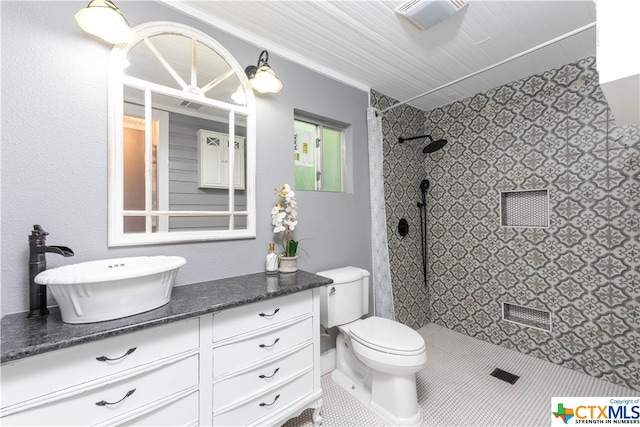 bathroom with toilet, vanity, tile patterned floors, and tiled shower