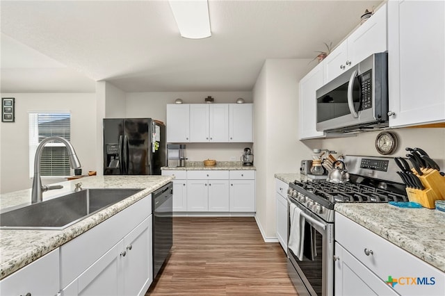 kitchen featuring hardwood / wood-style flooring, white cabinetry, sink, black appliances, and light stone counters