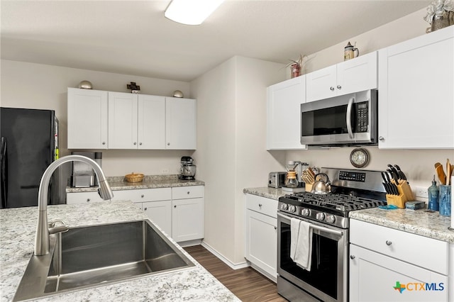 kitchen with stainless steel appliances, dark wood-type flooring, sink, light stone countertops, and white cabinetry