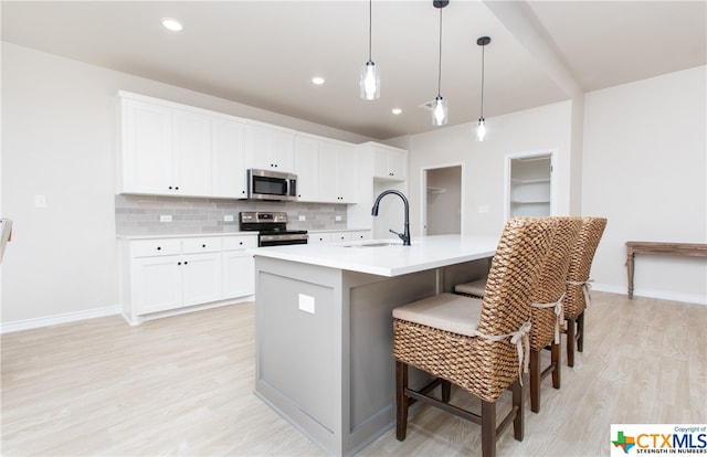 kitchen with stainless steel appliances, a center island with sink, sink, tasteful backsplash, and decorative light fixtures