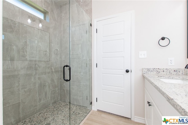 bathroom with hardwood / wood-style floors, a shower with door, and vanity