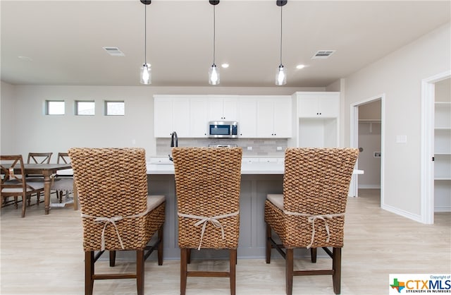 kitchen with a breakfast bar area, backsplash, decorative light fixtures, light hardwood / wood-style flooring, and white cabinets