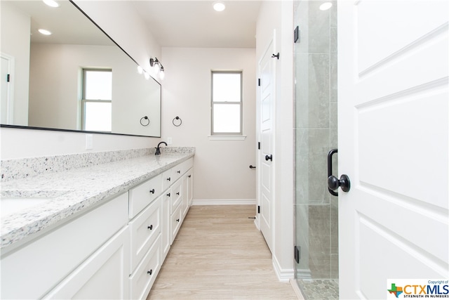 bathroom with a shower with door, plenty of natural light, wood-type flooring, and vanity