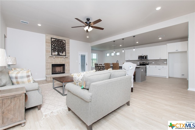 living room featuring ceiling fan, light hardwood / wood-style floors, and a fireplace