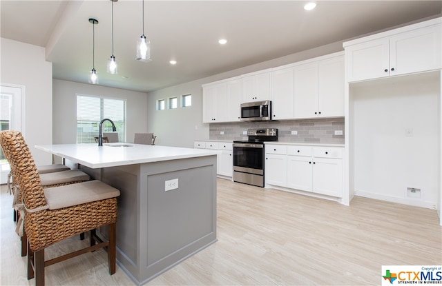 kitchen featuring light hardwood / wood-style floors, sink, a kitchen island with sink, pendant lighting, and appliances with stainless steel finishes