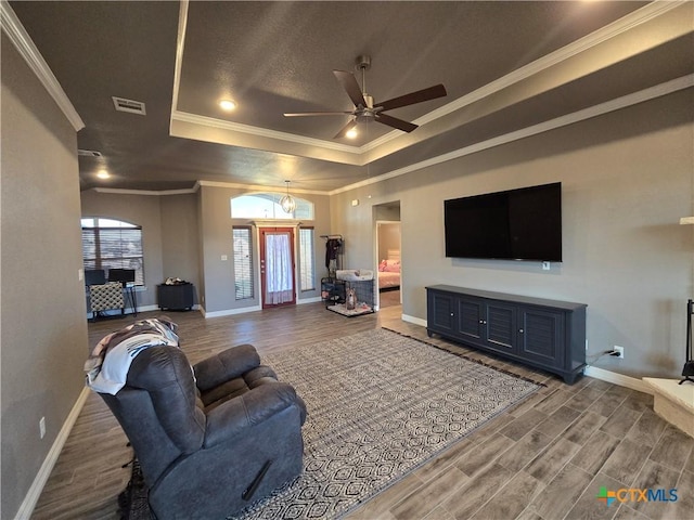 living room featuring hardwood / wood-style flooring, a tray ceiling, crown molding, and ceiling fan