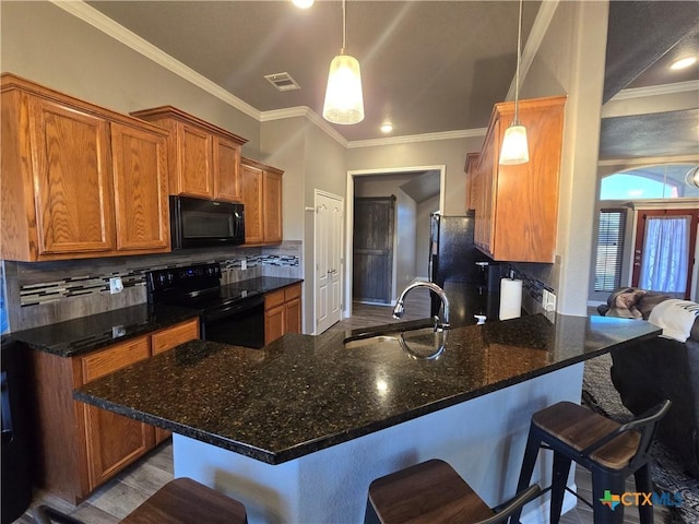 kitchen featuring decorative light fixtures, black appliances, decorative backsplash, sink, and a breakfast bar area