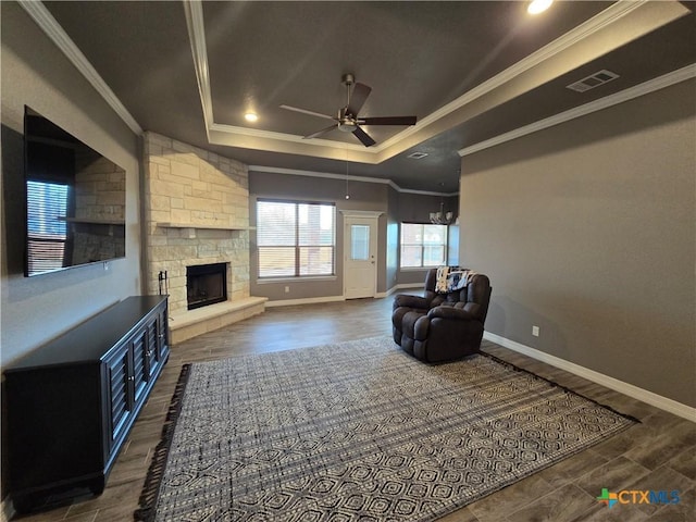 living room featuring ceiling fan, dark hardwood / wood-style floors, a tray ceiling, a fireplace, and ornamental molding