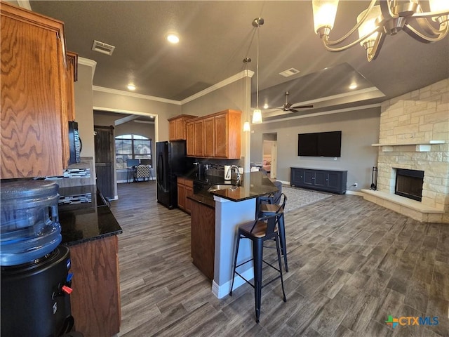 kitchen with a fireplace, black fridge, kitchen peninsula, ornamental molding, and dark hardwood / wood-style flooring