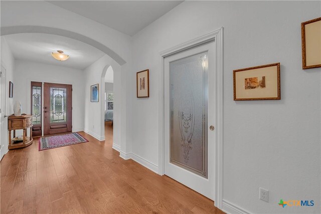 entrance foyer with arched walkways, light wood finished floors, and baseboards