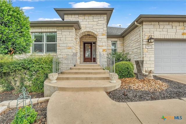 doorway to property with concrete driveway, roof with shingles, stone siding, and a garage