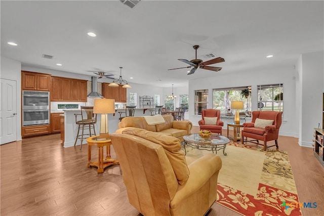 living room with ceiling fan with notable chandelier, visible vents, recessed lighting, and light wood-type flooring