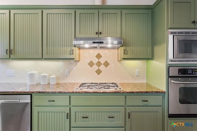 kitchen with light stone countertops, backsplash, stainless steel appliances, and green cabinetry