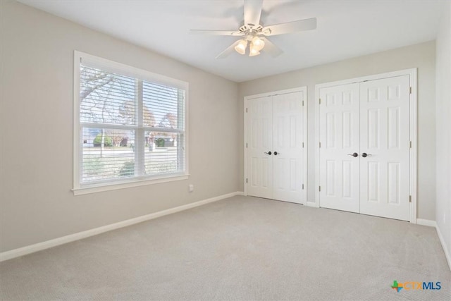 unfurnished bedroom with ceiling fan, light colored carpet, and two closets