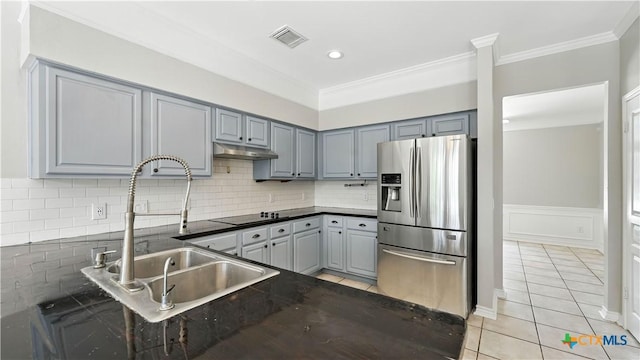 kitchen featuring stainless steel fridge, dark countertops, under cabinet range hood, ornamental molding, and light tile patterned floors