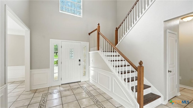 entryway with a high ceiling, healthy amount of natural light, stairs, and wainscoting