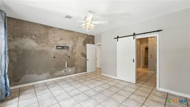 unfurnished bedroom featuring a barn door, an accent wall, ceiling fan, and tile patterned floors