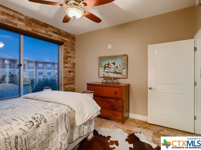 bedroom featuring ceiling fan and brick wall